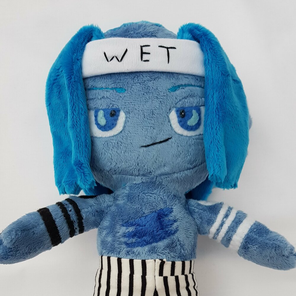 a plush of a blue man with dark blue hair wearing black and white stripy trousers and with black and white tattoos on his arms, wearing striped trousers